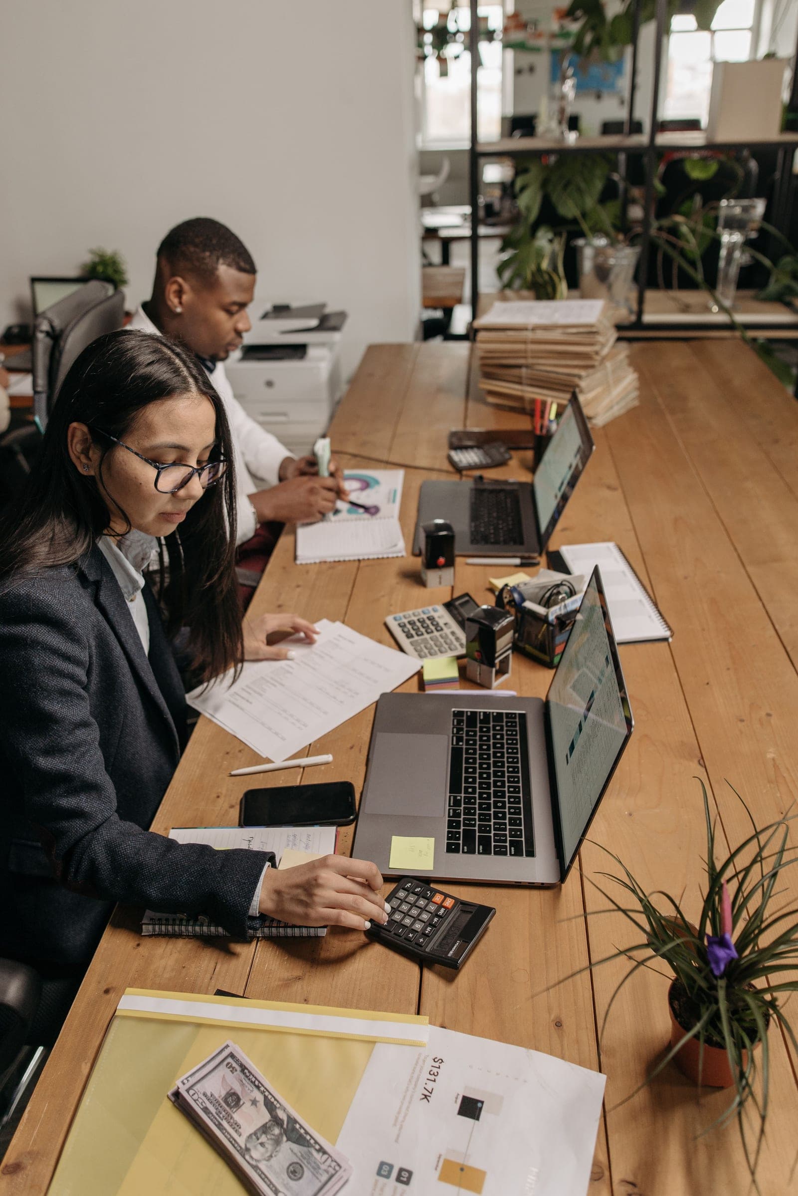 A desk with a laptop, calculator and cash as someone works through payments